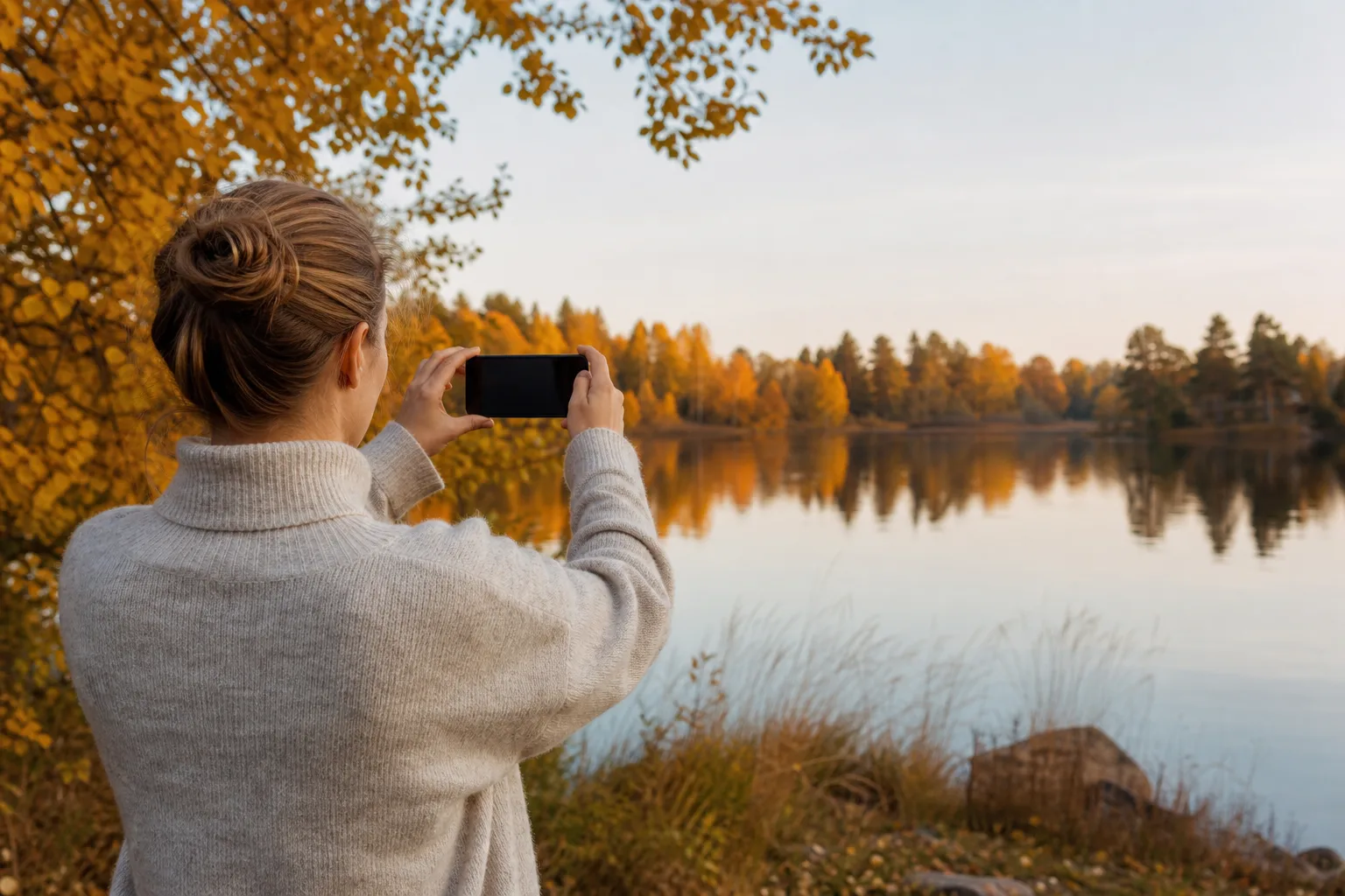 Person fotograferar en sjö i nordiskt höstljus med en mobiltelefon – billig Google Pixel med abonnemang